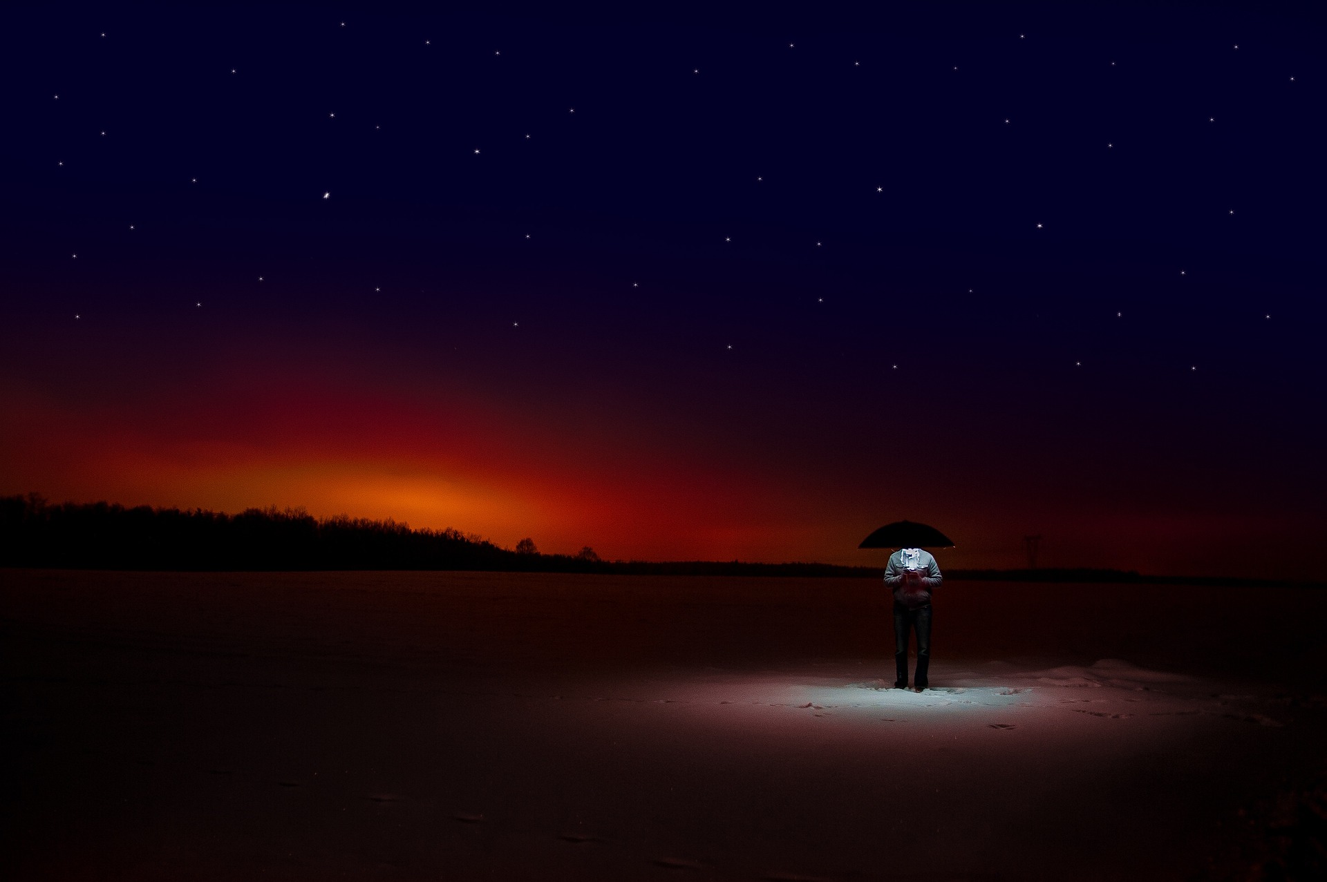 A man standing in the middle of nowhere, at night, illuminated by the light he holds in his hand.